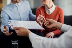 Close-up of woman signing an agreement with insurance agent while being on a meeting with her husband.